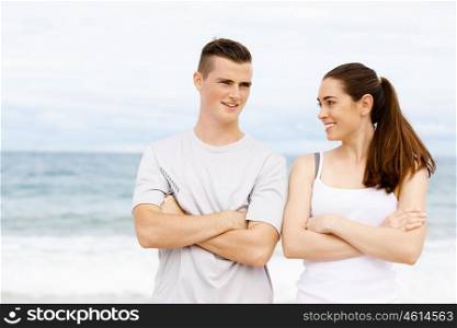 Young couple looking at each other on beach. Young couple looking at each other while standing on beach in sports wear