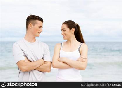 Young couple looking at each other on beach. Young couple looking at each other while standing on beach in sports wear
