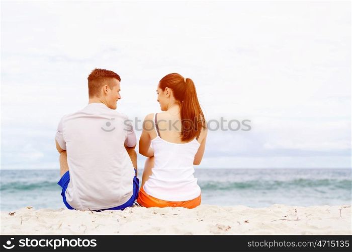 Young couple looking at each other while sitting on beach. Young couple looking at each other while sitting together on beach