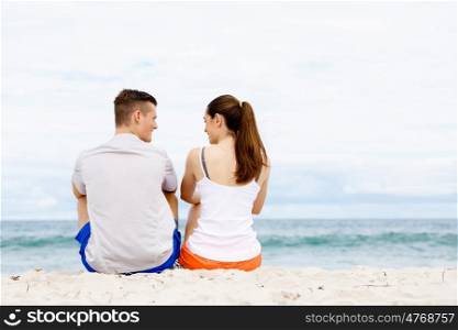Young couple looking at each other while sitting on beach. Young couple looking at each other while sitting together on beach in sports wear