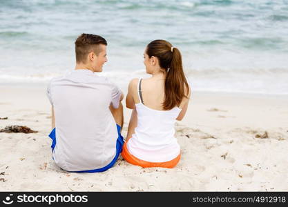 Young couple looking at each other while sitting on beach. Young couple looking at each other while sitting together on beach in sports wear