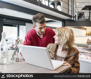 Young couple looking at each other while using laptop in cafe