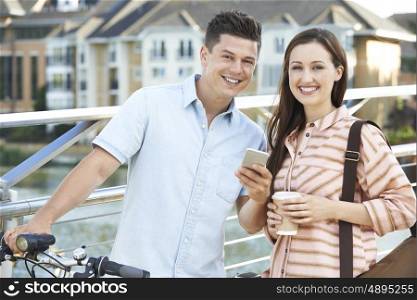 Young Couple Looking At Phone On Way To Work In Urban Setting