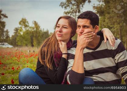Young couple looking away with a thoughtful look while sitting on the grass in a field of red poppies.