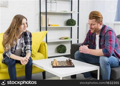 young couple looking each other with chess board white table