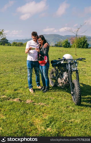 Young couple looking mobile with a motorcycle outdoors. Couple looking mobile with a motorcycle