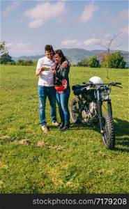Young couple looking mobile with a motorcycle outdoors. Couple looking mobile with a motorcycle