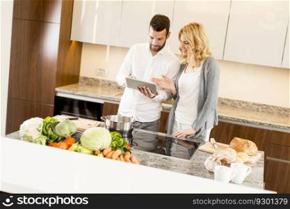 Young couple looking tatablet in the kitchen while preparing meals