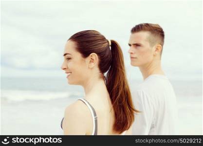 Young couple looking thoughtful while standing next to each other on beach. Young couple looking thoughtful while standing next to each other on beach in sports wear