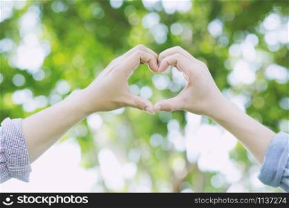 Young couple lover show holding hands make heart shape over in public parks.