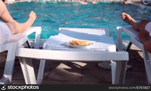 young couple lying beside the swimming pool eating crisps