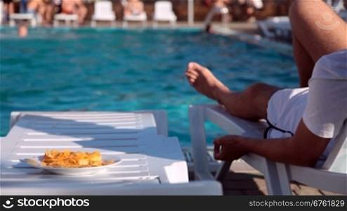 young couple lying beside the swimming pool eating crisps