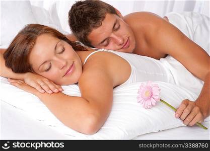 Young couple lying in bed, man holding Gerber daisy