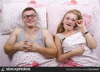 Young couple lying in bed. On each dressed round funny glasses. Top view