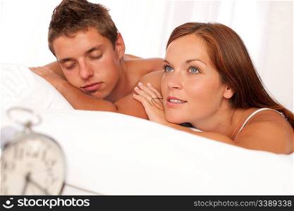 Young couple lying in white bed with silver alarm clock