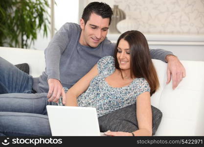 Young couple lying on a sofa with a laptop