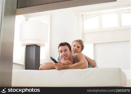 Young couple lying on bed and watching TV
