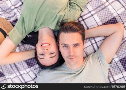 Young couple lying on blanket on grass. Woman with her boyfriend relaxing on picnic blanket outdoors. Family portrait in love lying on grass with copy space.. Picnic time. Young couple having fun on picnic in the park.