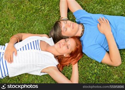Young couple lying on grass closed eyes enjoy summertime top-view