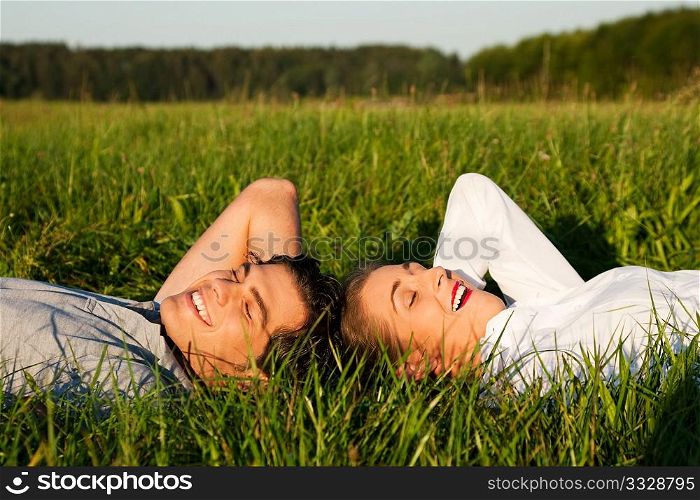 Young couple lying together on a green meadow in summer in the sunshine having eyes closed taking a nap