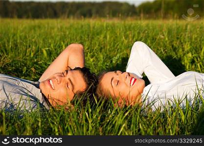 Young couple lying together on a green meadow in summer in the sunshine having eyes closed taking a nap