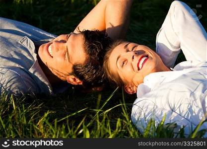 Young couple lying together on a green meadow in summer in the sunshine