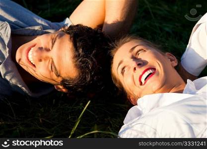 Young couple lying together on a green meadow in summer in the sunshine