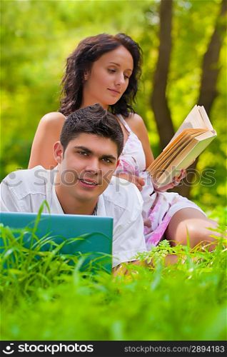 Young couple lying with laptop and book at park
