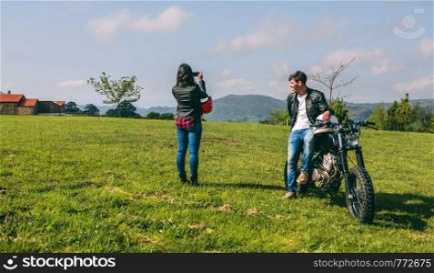 Young couple making a landscape photo during a stop of a motorcycle trip. Couple making a landscape photo during a motorcycle trip