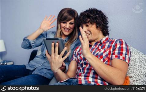 Young couple making a video call with the tablet sitting on the bed