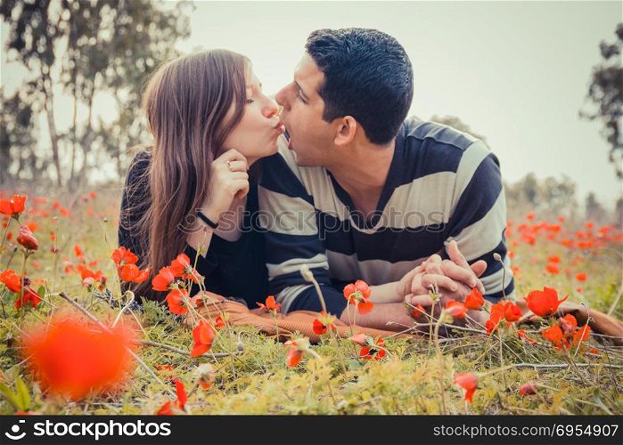 Young couple making silly faces to each other while they laying on the grass in a field of red poppies.
