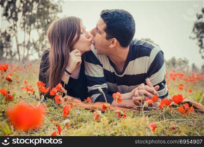 Young couple making silly faces to each other while they laying on the grass in a field of red poppies.