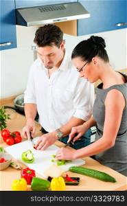Young couple - man and woman - cooking in their kitchen at home preparing vegetables for salad and pasta sauce