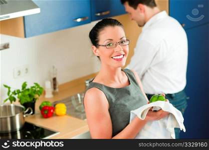 Young couple - man and woman - cooking in their kitchen at home cleaning vegetables