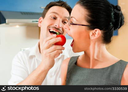 Young couple - man and woman - cooking in their kitchen at home, they teasing each other