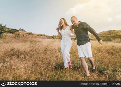 Young couple man and woman in love walking on the field on the mountain in autumn or summer day hugging together having fun bonding flirting flirt husband and wife lovers