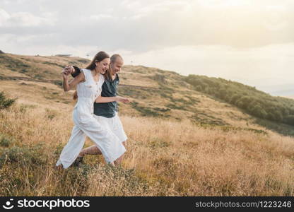 Young couple man and woman in love walking on the field on the mountain in autumn or summer day hugging together having fun bonding flirting flirt husband and wife lovers