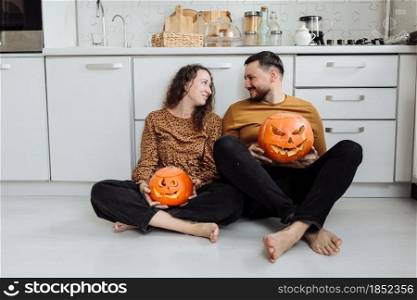 Young couple man and woman sitting on the floor at kitchen at home having fun and preparing for halloween talking laughing cheerful.. Young couple man and woman sitting on the floor at kitchen at home having fun and preparing for halloween talking laughing cheerful