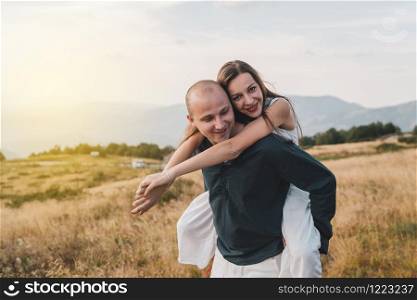 Young couple married in love man and woman young girl boyfriend husband is holding her on the mountain range in nature in summer or autumn day while she hug him from the back