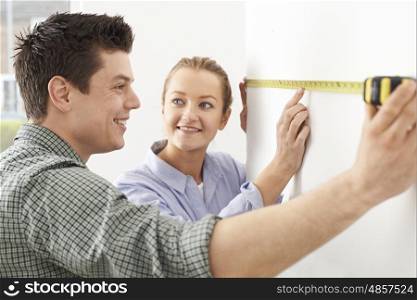 Young Couple Measuring Wall In New Home