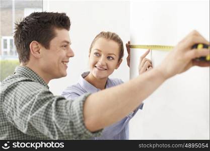 Young Couple Measuring Wall In New Home