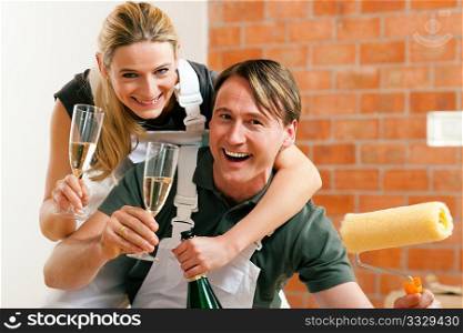 Young couple moving in new flat doing renovation and painting, celebrating their new home with sparkling wine