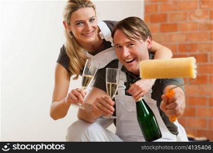 Young couple moving in new flat doing renovation and painting, celebrating their new home with sparkling wine