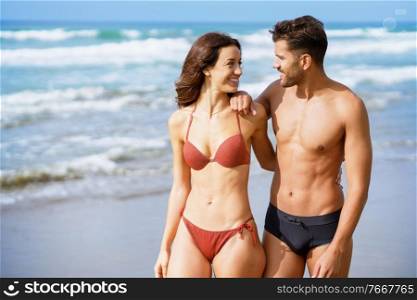 Young couple of beautiful athletic bodies walking together on the beach enjoying their holiday at sea. Young couple of beautiful athletic bodies walking together on the beach