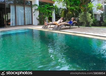 young couple of people relax on villa by swimming pool