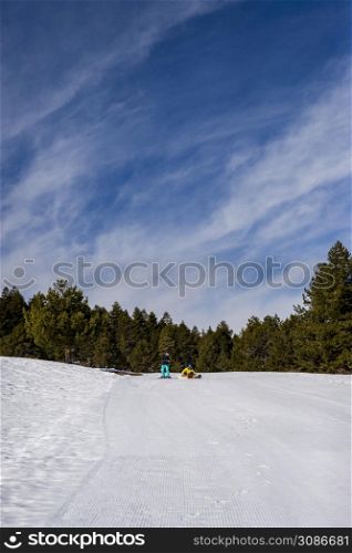 Young couple of skiers man and woman unrecognizable in snowboarding equipment masks far away on the background of snow-capped mountains high at a ski resort on a sunny day