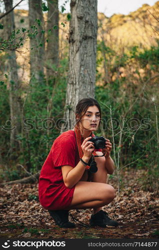 Young couple of women wearing dresses reading a book and taking photos with old camera in the forest with their horse.