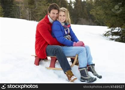 Young Couple On A Sled In Alpine Snow Scene