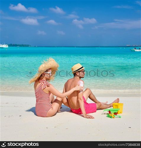 Young couple on beach. Woman applying sun screen protection lotion on man&rsquo;s back. Summer vacation at Maldives.