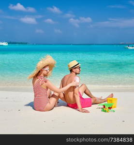 Young couple on beach. Woman applying sun screen protection lotion on man&rsquo;s back. Summer vacation at Maldives.